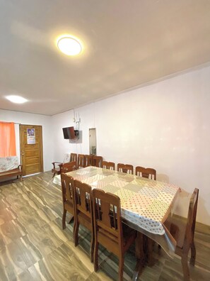 Un coin repas comprenant une grande table, des chaises, une porte en bois et un téléviseur fixé au mur.