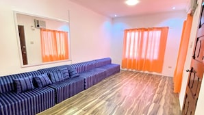 Ein Zimmer mit einer Couch, einem Spiegel, einer Deckenleuchte und orangefarbenen Vorhängen.