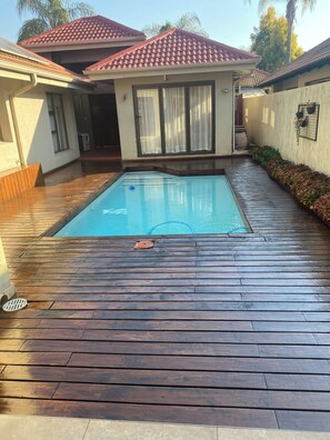 A swimming pool with a wooden deck, a house with a red-tiled roof, and a small garden area. - Pecanwood Picturesque Peaceful (Hartbeespoort)