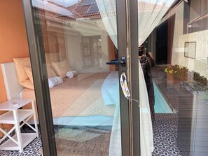 A room with a bed, a small table, and a chair, a glass door, and a view of the outside. - Pecanwood Picturesque Peaceful (Hartbeespoort)