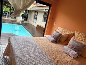 A bedroom with a view of a swimming pool, a bed with a quilted cover, and two pillows with floral designs. - Pecanwood Picturesque Peaceful (Hartbeespoort)