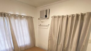 A small, single-bed room with a wooden floor, a small table, and a wall-mounted air conditioner. - Simple, Practical & Comfy Room 4 (General Luna)