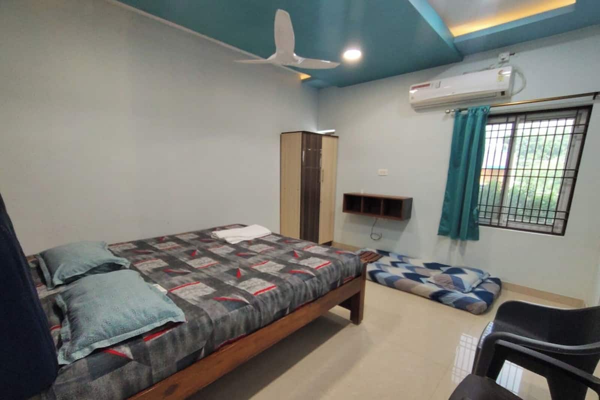 A bedroom with a bed, a chair, a wardrobe, a shelf, and an air conditioning unit.