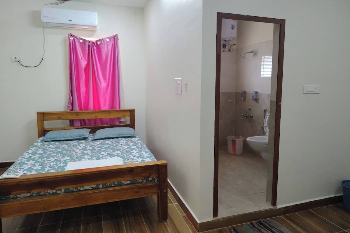 A bedroom with a bed, a ceiling fan, an air conditioner, a bathroom visible through a mirror, and a tiled floor.