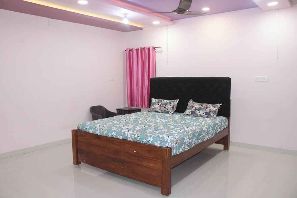A bedroom with a wooden bed, a desk, a chair, a pink curtain, and a ceiling fan.