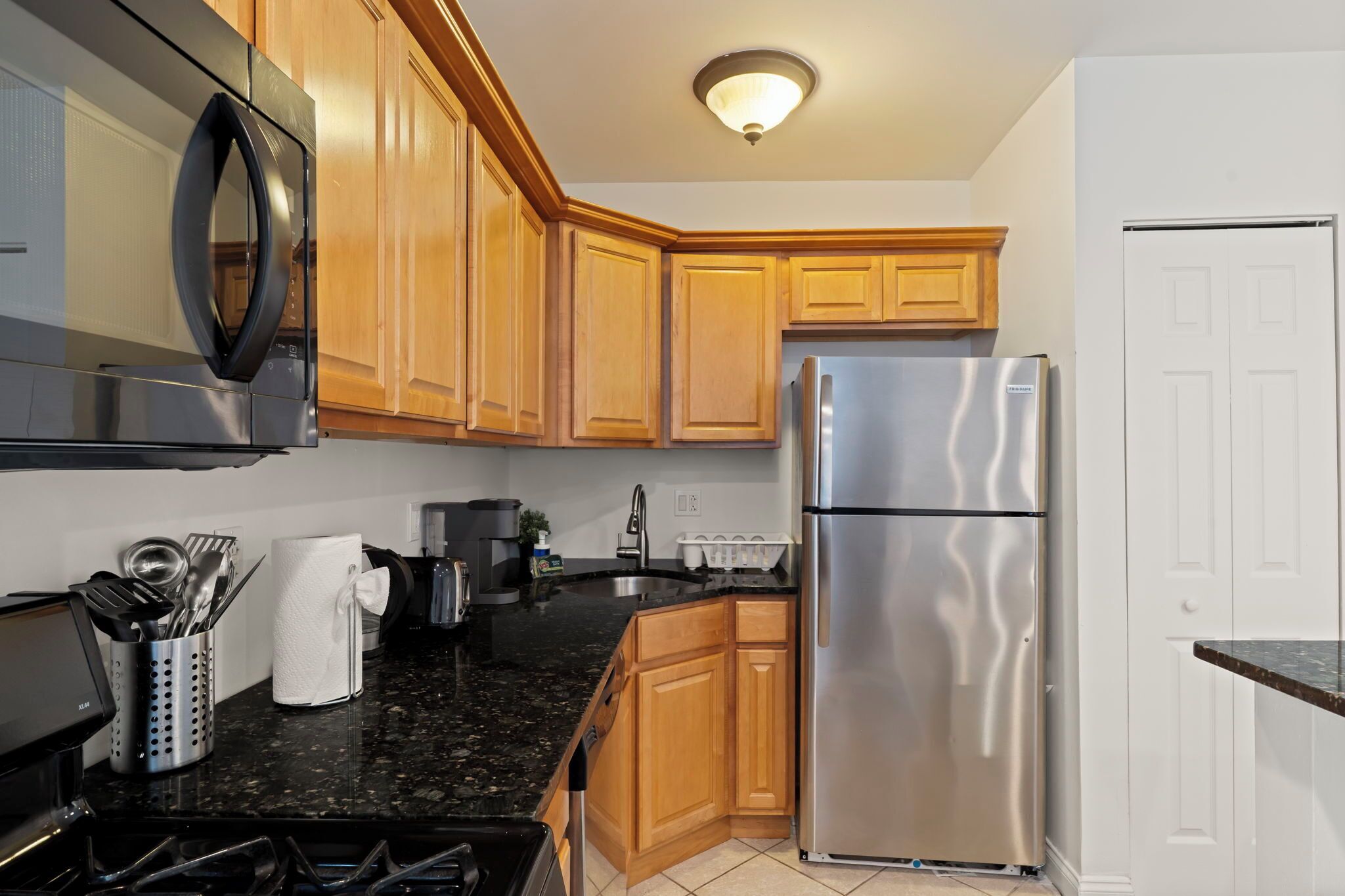 A kitchen with wooden cabinets, a stainless steel refrigerator, a microwave, and a stove.