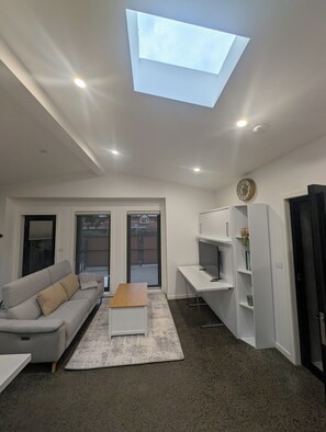 A modern living room with a sofa, coffee table, and a desk. - Architectural Coastal Retreat (Williamstown North)