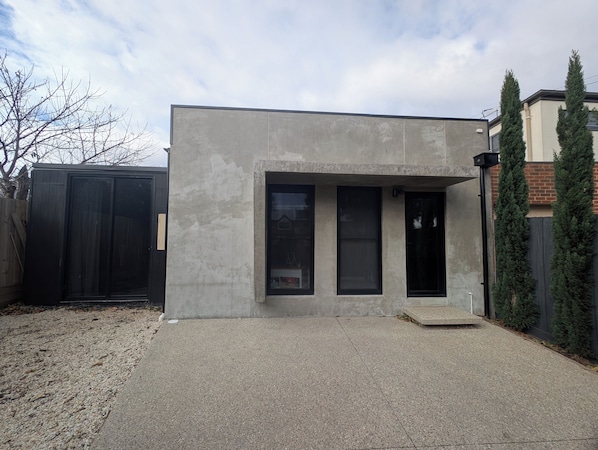 A modern building with a concrete facade, large windows, and a gravel driveway.