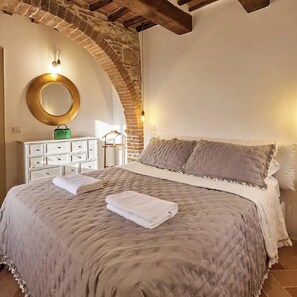 Una camera da letto con un letto grande, una cassettiera, uno specchio e un arco in pietra.