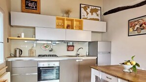 A compact kitchen with modern appliances, a wooden dining table, and clear chairs.
