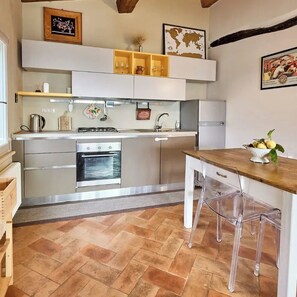 A compact kitchen with modern appliances, a wooden dining table, and clear chairs.