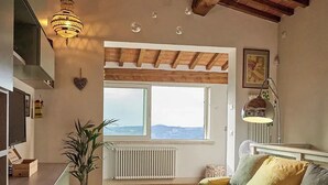 A cozy living room with a sofa, a potted plant, a radiator, and a large window with a view.