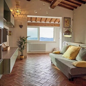 A cozy living room with a sofa, a potted plant, a radiator, and a large window with a view.