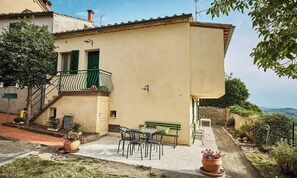 Un edificio a due piani con un balcone, un tavolo e sedie all'esterno e un muro in pietra.
