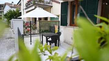 Un patio con una mesa, sillas, un paraguas blanco y una cerca adornada con flores.