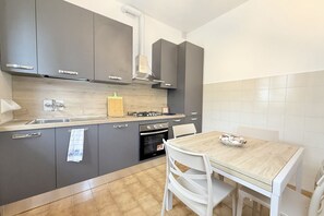 Eine moderne Küche mit grauen Schränken, einer Holzarbeitsplatte, einem Gasherd, einem Backofen und einem Esstisch mit Stühlen.