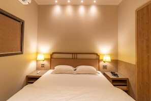 Habitación de hotel con una cama grande, dos mesitas de noche con lámparas, un cabecero de madera y una puerta de madera.