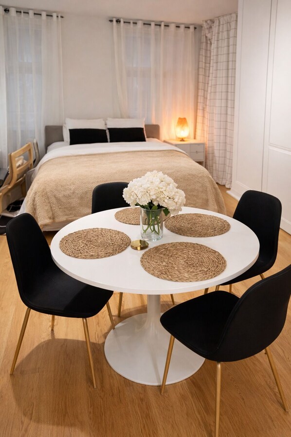 A hotel room with a bed, a bedside table with a lamp, a round dining table with chairs, and a vase with flowers.