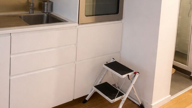 A modern kitchen with white cabinets, a stainless steel oven, a sink, and a small step stool.