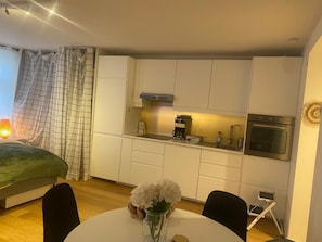 Een kleine keuken met witte kastjes, een koffiezetapparaat en een oven.