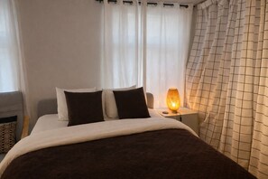 Un lit bien fait, recouvert d’une couverture marron foncé, avec des oreillers blancs et une lampe de chevet.