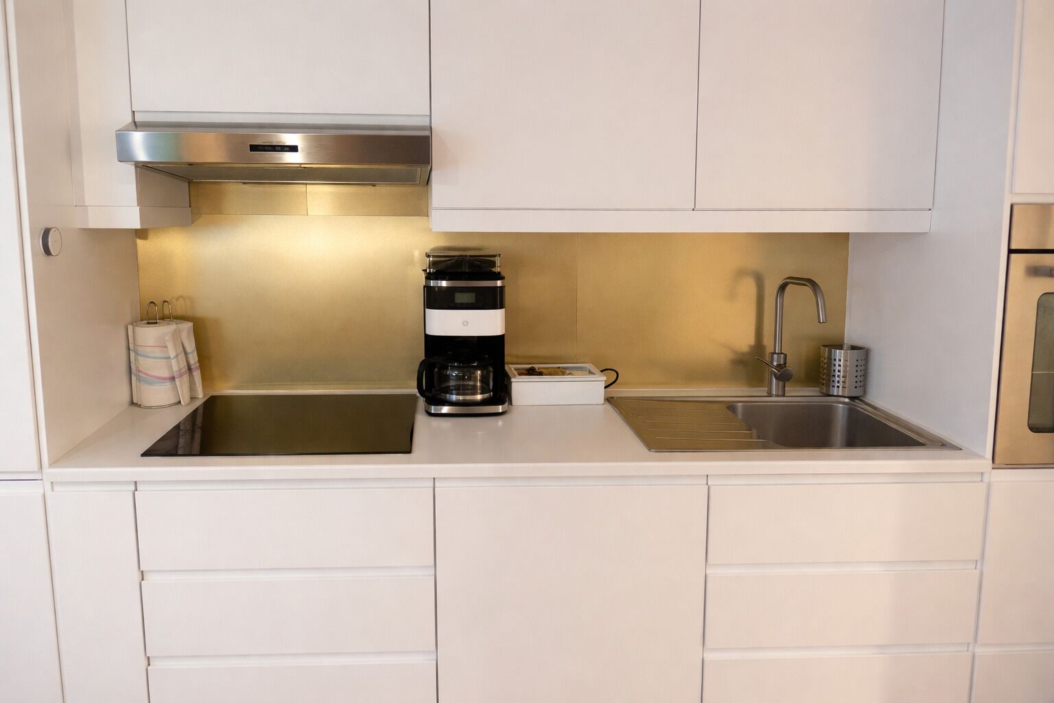 A kitchen with white cabinets, a stainless steel sink, a coffee maker, and a built-in range hood.