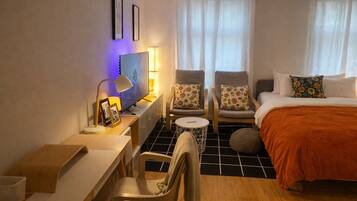 Ein Hotelzimmer mit einem Bett, zwei Sesseln, einem Schreibtisch mit Computer, einem Fernseher und einer Lampe.