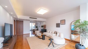 Una sala de estar moderna con un sofá modular, un televisor de pantalla plana, una mesa de centro y una planta grande en maceta.