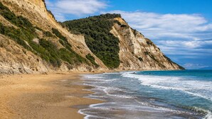 Una playa costera con una orilla arenosa y un acantilado escarpado con vegetación escasa.