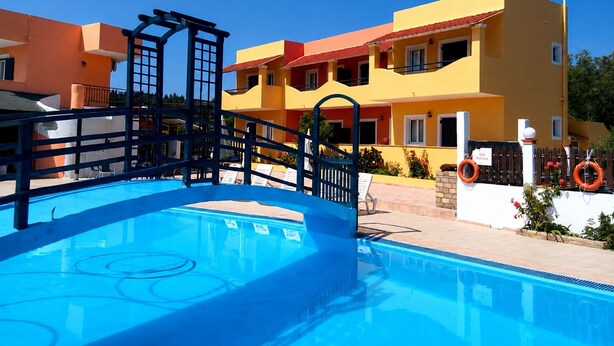 Una piscina con plataforma azul, un puente de madera y un edificio amarillo con balcones.