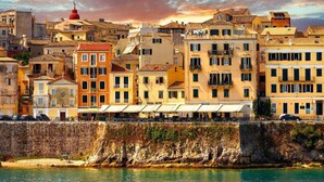Un paisaje urbano costero con edificios históricos, una cúpula roja destacada y un muro de piedra junto al agua.