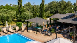 A swimming pool with lounge chairs and umbrellas, surrounded by greenery and shaded areas. - Nikos Villas - Poolside Escape in Kavos, Corfu (Corfu)