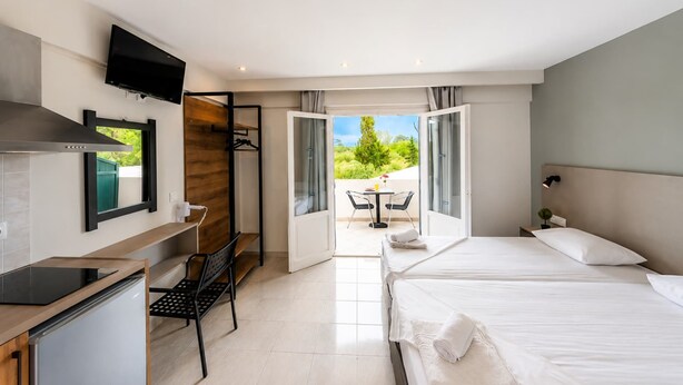 A hotel room with a bed, desk, TV, and a view of the outdoors. - Nikos Villas - Poolside Escape in Kavos, Corfu (Corfu)