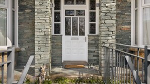 A stone facade with a white door, a metal railing, and a doormat. - Lakeside Studio Ridgestone (Windermere)