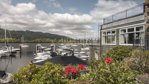 A marina with boats docked, a building with large windows, and a mountainous backdrop. - Lakeside Studio Ridgestone (Windermere)