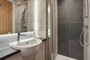 A bathroom with a white sink, a glass shower enclosure, and grey tiled walls. - Mereside Apartment Ridgestone (Windermere)