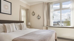 A bedroom with a large bed, a window with curtains, a radiator, and a framed picture on the wall. - Mereside Apartment Ridgestone (Windermere)