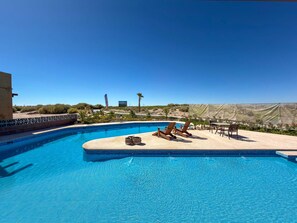 Una piscina con sillones de descanso, una mesa y vistas del paisaje circundante.