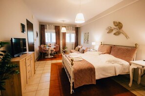 Una habitación de hotel con cama, mesita de noche, televisor, escritorio, silla y cortinas.