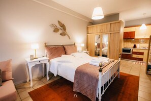 Un dormitorio con cama, mesitas de noche, armario y una cocina al fondo.