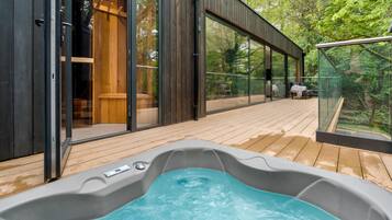 Un área moderna de hidromasaje al aire libre con un deck de madera, puertas correderas de vidrio grandes y vistas al bosque circundante.
