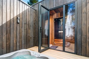 Un espacio de spa de madera con un jacuzzi, puertas de vidrio que dan a un vestuario y una terraza de madera.