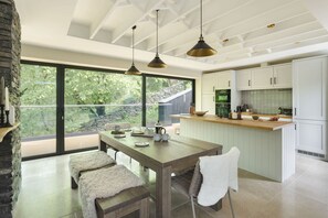 A modern kitchen with a large island, pendant lighting, and a view of greenery through large windows. - Fawns Keep - Hot Tub Sauna Retreat Ridgestone (Windermere)
