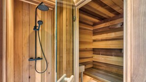 Uma sauna de madeira com porta de vidro, chuveiro e banco.