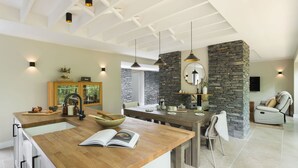 Cozinha moderna com ilha de madeira, detalhes em pedra, iluminação pendente e área de refeições com lareira de pedra.