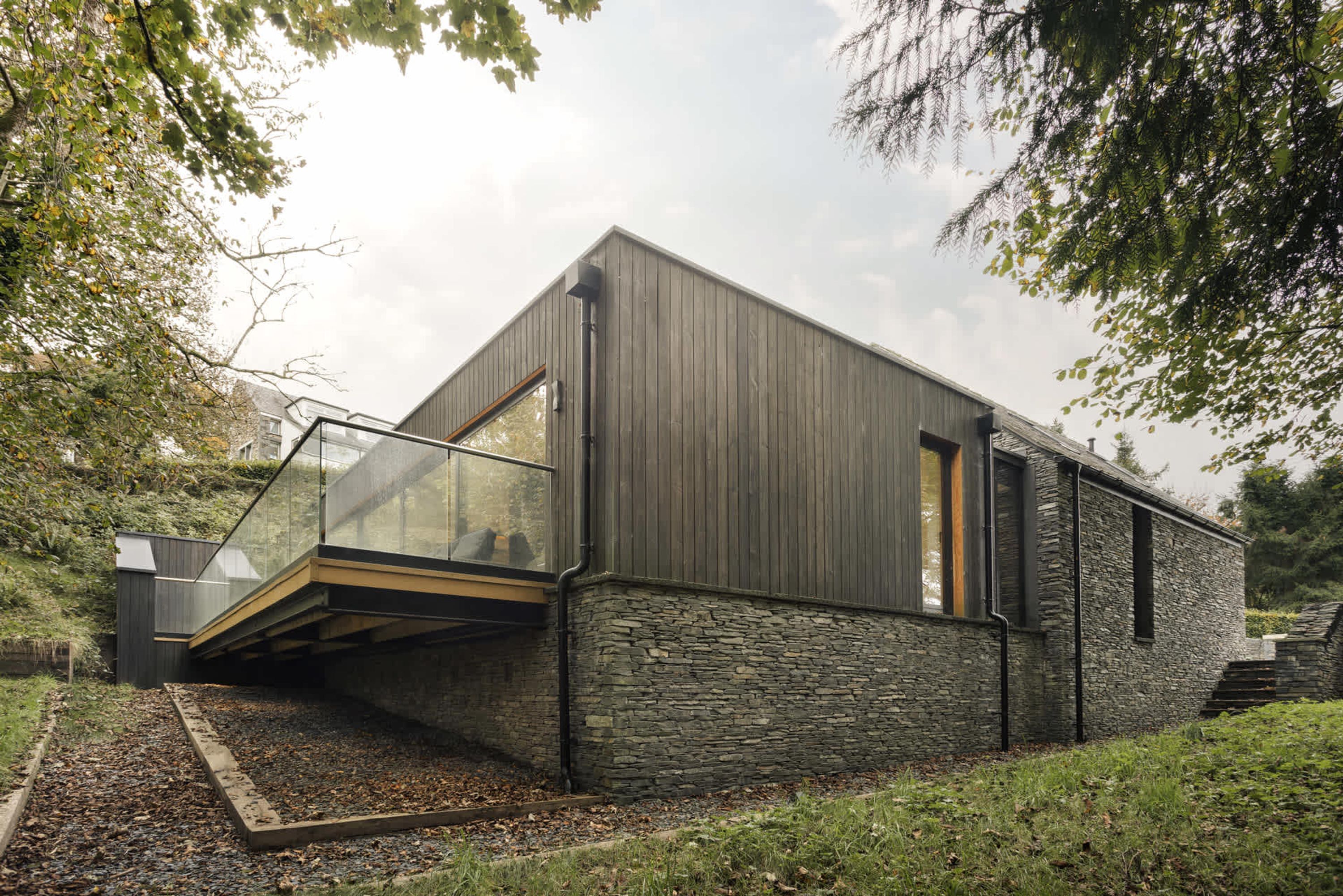 Una casa moderna con fachada de piedra, balcón de cristal y terraza de madera.