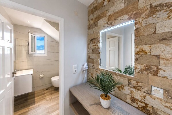 Ein Badezimmer mit Steinwand, Spiegel, Topfpflanze und Toilette.
