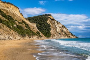 Ein Küstenstrand mit sandigem Ufer und einer steilen Klippe mit spärlicher Vegetation.