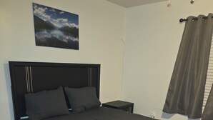 Ein Schlafzimmer mit einem Bett, einem Nachttisch, einem Wandbild und einem Fenster mit Vorhängen.