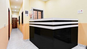 A hotel reception area with a reception desk, a door with a decorative design, and a wall-mounted light switch. - Classic Chowdhury Guest House (Barakpur)
